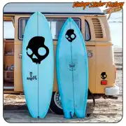 Adhésif avec motif de crâne noir appliqué sur deux planches de surf près d’un van