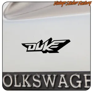 Logo Duke noir appliqué sur l’arrière d’un véhicule, à côté d’une plaque d’immatriculation