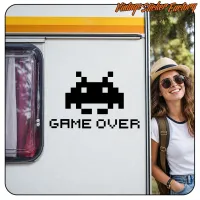 Aplicación de la pegatina «GAME OVER» con invasor espacial pixelado en una caravana, junto a una persona