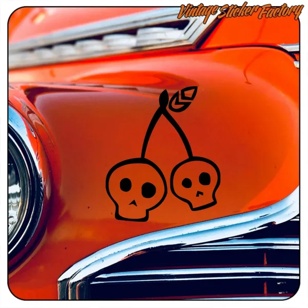 Detalle de dos calaveras unidas por tallos de cereza sobre un automóvil clásico naranja