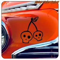 Detail von zwei durch Kirschstiele verbundenen Totenköpfen auf einem orangefarbenen Oldtimer