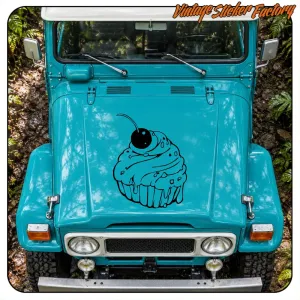 Black cupcake with cherry applied to the hood of a turquoise off-road vehicle