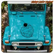 Cupcake noir avec cerise posé sur le capot d'un véhicule tout-terrain turquoise