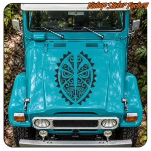 Masque tiki noir appliqué sur le capot d’un véhicule turquoise