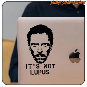 Adhesivo con rostro barbado y texto «IT'S NOT LUPUS» aplicado en la tapa de un portátil