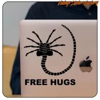 Detalle del diseño arácnido con cola curvada y texto «FREE HUGS» sobre un portátil
