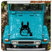 Adhesivo de Totoro y dos figuras pequeñas aplicado sobre el capó de un vehículo turquesa